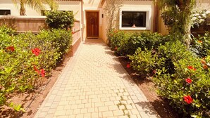 A pathway leading to a building with a door and window, surrounded by greenery and red flowers. - Villa Eden L'Orangeraie Dyar Shemsi Agadir (Taroudant)