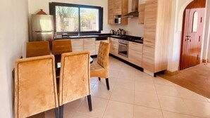 A modern kitchen with wooden cabinets, a dining area with two chairs, and a large window. - Villa Eden L'Orangeraie Dyar Shemsi Agadir (Taroudant)