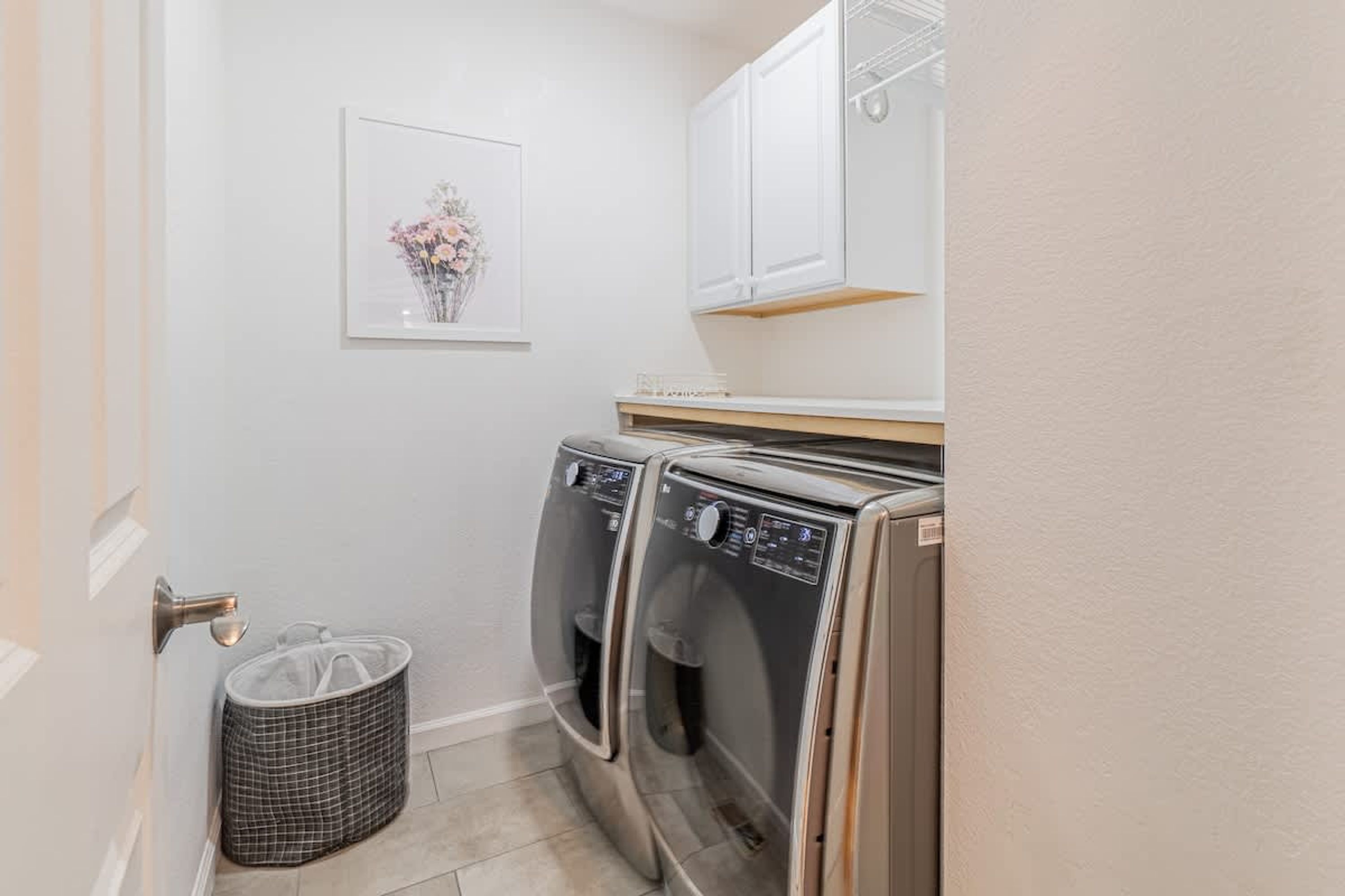 A laundry area with two front-loading washing machines, a drying rack, and a trash bin.