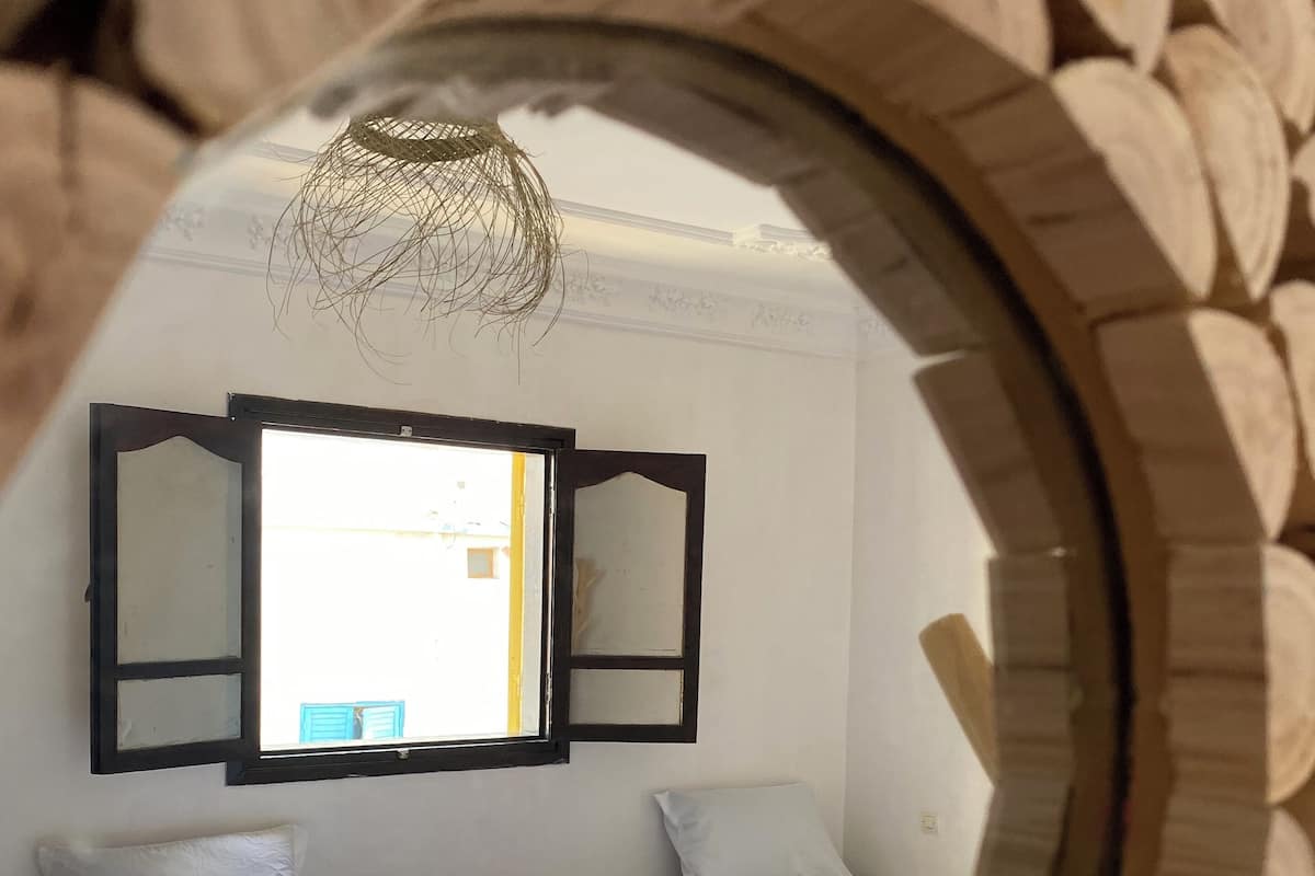 A bedroom with two beds, a window, and a mirror reflecting the room.