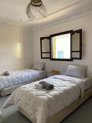 A room with two beds, a window with open shutters, and a hanging light fixture. - TITRYTE SURF HOUSE (Agadir)
