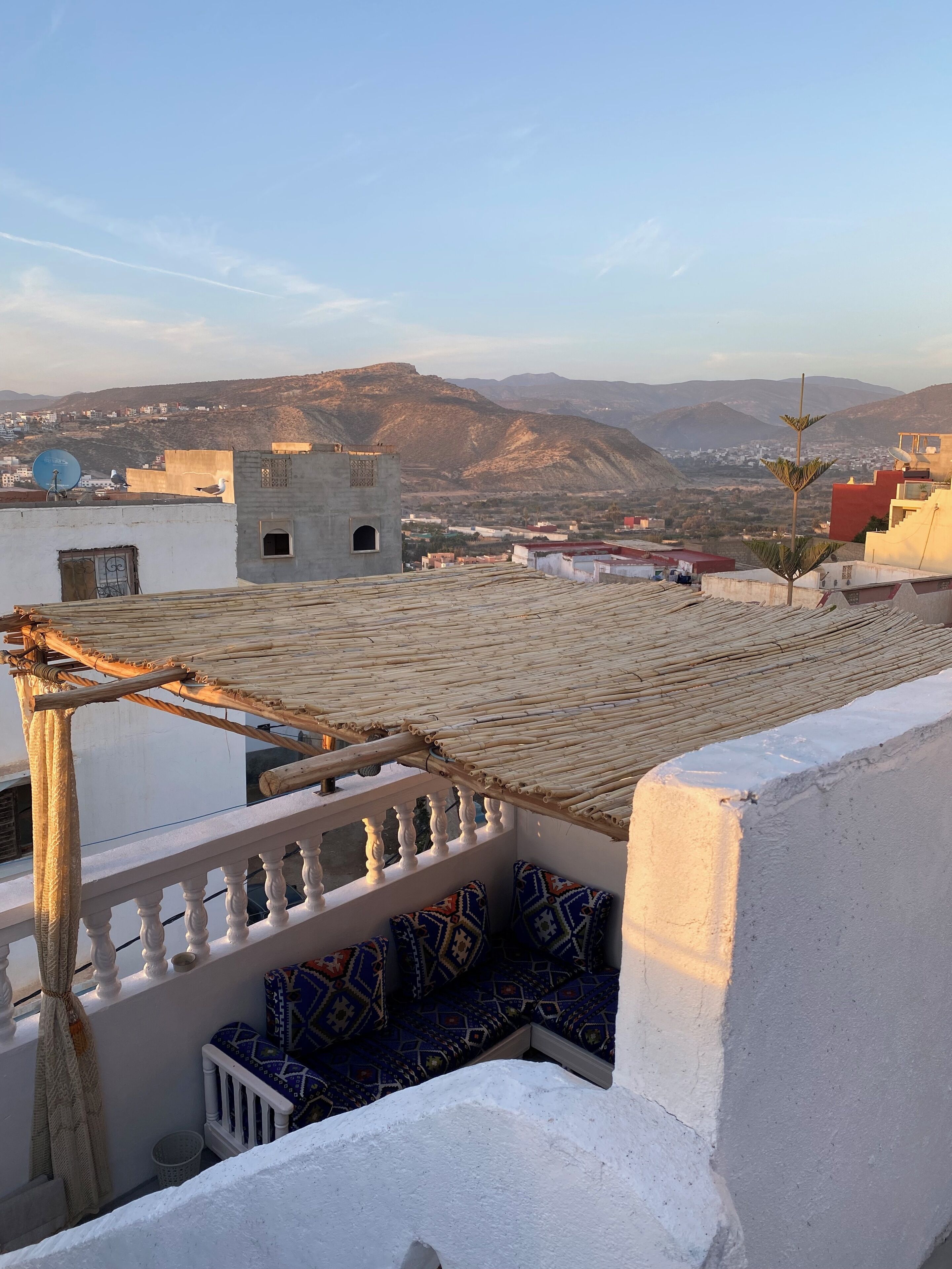 A rooftop terrace with a view of distant mountains, a small building, and a clear sky.