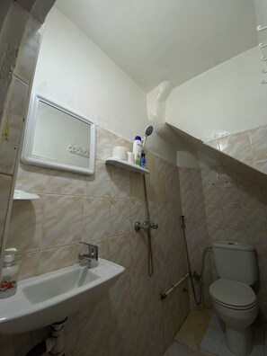 A bathroom with a sink, toilet, and shower. There is a shelf with toiletries and a mirror above the sink. - TITRYTE SURF HOUSE (Agadir)