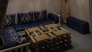 A cozy room with a wooden ceiling, a woven wall hanging, a surfboard, and a patterned sofa. - TITRYTE SURF HOUSE (Agadir)