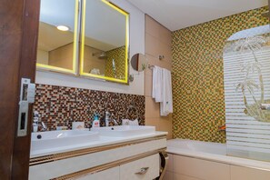 Casa de banho com duas pias, espelho, chuveiro e parede revestida a azulejos.