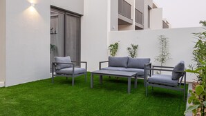 Ein zeitgemäßer Außenbereich mit einer Sitzecke, einer Couch und Sesseln, einem kleinen Tisch und einer Wandleuchte.