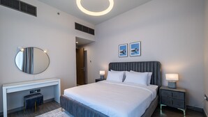 A modern bedroom with a large bed, a round mirror, a desk, and two bedside tables with lamps. - MBL Residence 1205 jlt (Dubai)