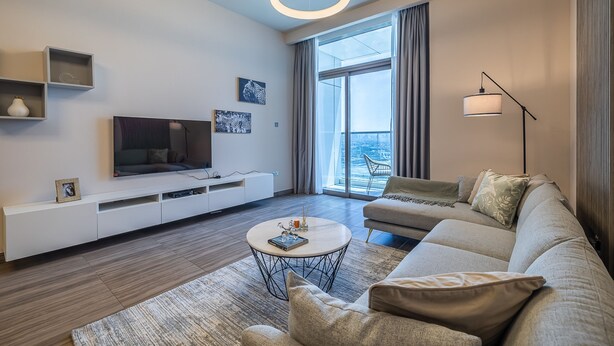 A modern living room with a sofa, a coffee table, a TV, and a large window with curtains. - MBL Residence 1205 jlt (Dubai)