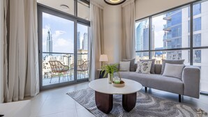 Una sala de estar moderna con un sofá, una mesa de centro redonda y vistas a un paisaje urbano a través de grandes ventanales.
