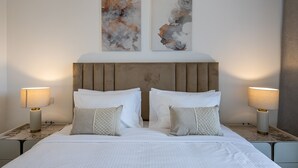 Una habitación de hotel con una cama grande, dos mesitas de noche con lámparas, un cabecero de madera y arte abstracto en la pared.