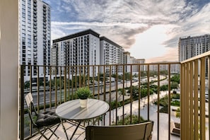 Ein Balkon mit rundem Tisch und Stühlen, mit Blick auf eine Skyline aus Hochhäusern und einer Straße.