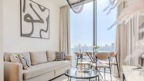 A modern living room with a sofa, a glass coffee table, and a view of a city skyline through large windows. - Sobha Waves 2915 in Dubai (Dubai)