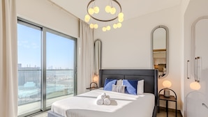 A modern hotel room with a large bed, two bedside tables, a large window with a city view, and a chandelier. - Sobha Waves 2915 in Dubai (Dubai)