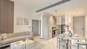 A modern living room with a sofa, coffee table, and dining area with chairs and a table set for a meal. - MAG Building 920 711 (Dubai)