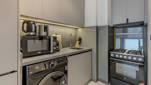 A compact kitchen with a washing machine, microwave, coffee maker, and gas stove. - MAG Building 920 711 (Dubai)