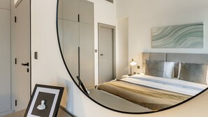 A bedroom with a bed, bedside table, lamp, and a framed picture on the wall. - MAG Building 920 711 (Dubai)