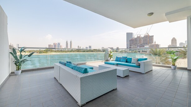 A modern outdoor lounge area with a city view, featuring a white sofa set and a dining table. - Azure Residences 117 Premium 2bdr Palm (Dubai)