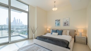 A modern bedroom with a large window, a bed with a gray blanket, two bedside tables with lamps, and a city view. - Azure Residences 117 Premium 2bdr Palm (Dubai)