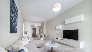 A modern living room with a large sofa, a TV, and a dining area in the background. - Azure Residences 117 Premium 2bdr Palm (Dubai)