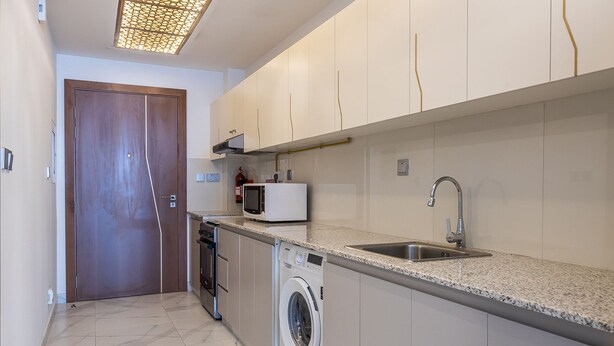 A compact kitchen with a washing machine, microwave, and sink. - Millennium Binghatti Studio - 1310 Business bay (Dubai)
