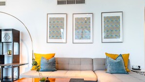 Una sala de estar moderna con un sofá gris, cojines amarillos y azules, una mesa de centro de madera y tres obras de arte enmarcadas en la pared.