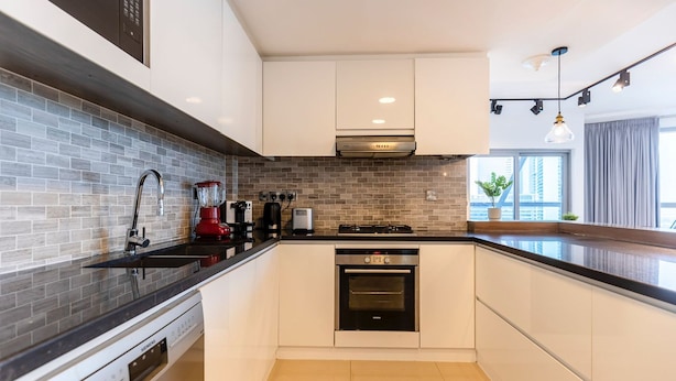Una cocina moderna con armarios blancos, encimera negra, horno integrado, cafetera y ventana con vistas a edificios.