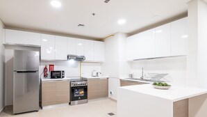 Uma cozinha moderna com armários brancos, geladeira de aço inoxidável, forno embutido e bancada branca.