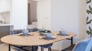 Uma área de refeições moderna com uma mesa de madeira redonda posta para dois, cercada por cadeiras estofadas em azul.