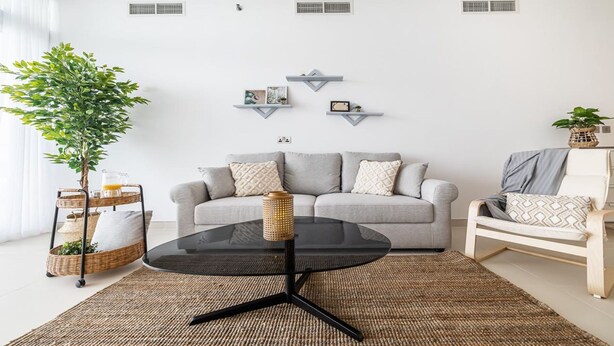 Een moderne woonkamer met een grijze bank, een zwarte salontafel en een rieten bijzettafeltje.