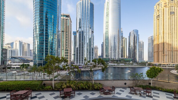 A modern cityscape with high-rise buildings, a waterfront, and outdoor seating areas. - Lake View Residence 208 (Dubai)