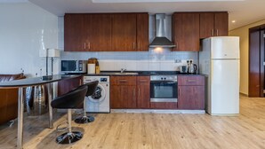 A modern kitchen with wooden cabinets, stainless steel appliances, a built-in oven, and a washing machine. - Lake View Residence 208 (Dubai)