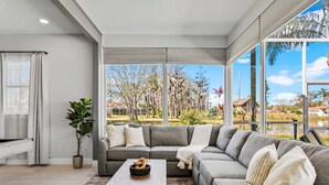 A modern living room with a sectional sofa, a coffee table, and a view of a residential area through large windows.