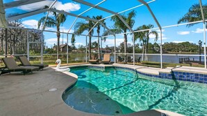 A swimming pool with a hot tub, lounge chairs, and a view of a lake and palm trees.