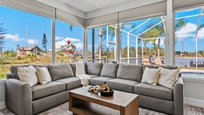 A modern living room with a sectional sofa, a wooden coffee table, and large windows offering a view of a residential area and a body of water.