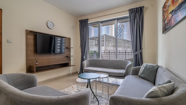 A modern living room with a flat-screen TV, grey sofas, a small coffee table, and a balcony with a view of tall buildings. - Standpoint Tower 1 606 (Dubai)