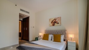 A hotel room with a large bed, two bedside tables with lamps, a painting of a horse on the wall, and a door leading to another room. - Standpoint Tower 1 606 (Dubai)