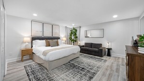 A modern bedroom with a large bed, bedside tables, a grey sofa, and a small side table with a lamp. - The Perfect Family Retreat w Pool and Games (Tampa)