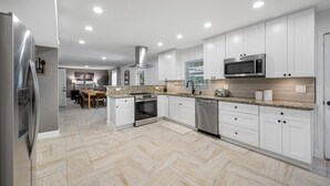 A modern kitchen with white cabinets, stainless steel appliances, and a herringbone floor pattern. - The Perfect Family Retreat w Pool and Games (Tampa)