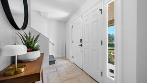 A hallway with a wooden console table, a potted plant, a mirror, and a set of white doors leading to an outdoor area. - The Perfect Family Retreat w Pool and Games (Tampa)