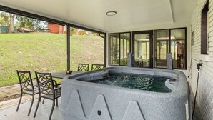 Un bain à remous situé dans un espace extérieur abrité, avec une table et des chaises, de grandes fenêtres et une pelouse.