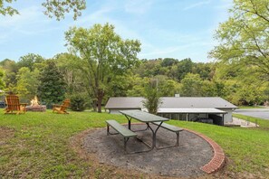 A picnic area with a table and benches, surrounded by trees and a building in the background.
