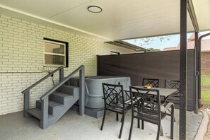 A covered outdoor area with a staircase, a table with chairs, and a large gray cylindrical object.