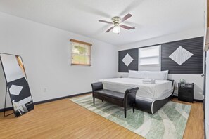 A bedroom with a bed, a nightstand, a chair, a ceiling fan, and a window with blinds.