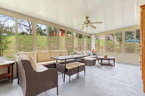 A covered patio area with wicker furniture, a ceiling fan, and large windows offering a view of the outdoors.