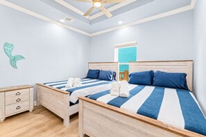 A bedroom with two beds, wooden headboards, a ceiling fan, and a decorative mermaid tail on the wall.