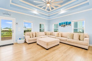 A spacious living room with a large L-shaped beige sofa, a wooden ceiling, and a view through a glass door. - Beach View | Hot Tub | Sleeps 14 + Hammock (Crystal Beach)