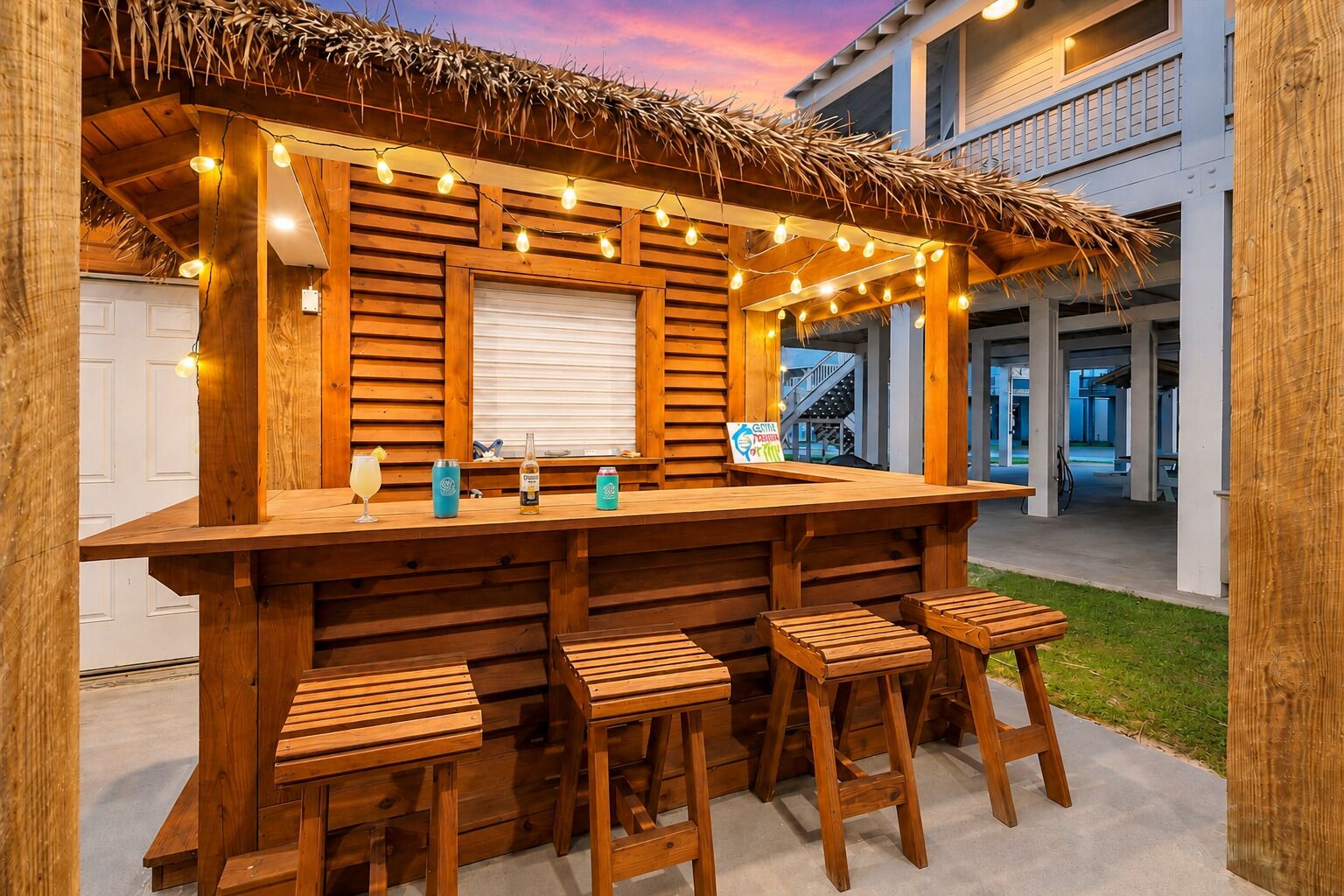Un área de bar al aire libre con taburetes de madera, una barra y luces colgantes.