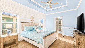 Une chambre à coucher avec un lit, une télévision, un ventilateur de plafond et une fenêtre.