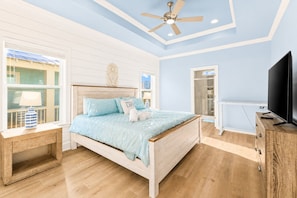 Una camera da letto con un letto, televisione, ventilatore a soffitto e una finestra.