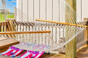 A hammock chair with a wooden frame and white netting, placed on a wooden deck with a wooden fence in the background.